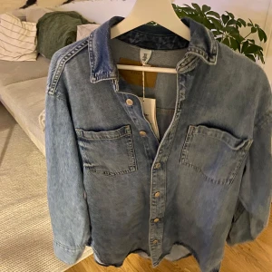 Jeans skjorta - Blå jeans skjorta (eller tunn jacka beroende på hur man vill ha den). Oversized i storleken. Sömmen inuti ärmen är felsydd och har släppt men det är inget som syns eller påverkar funktionen
