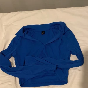 Blå ribbad tröja - Säljer en snygg blå ribbad tröja med långa ärmar och en unik krage. Perfekt för att hålla sig varm och stilren under kyligare dagar. Passar bra till både jeans och kjol.