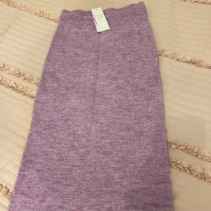 Lila stickad kjol från Lindex - Säljer en lila stickad kjol från Lindex i ullblandning. Perfekt för kyligare dagar. Kjolen har en enkel design som gör den lätt att matcha med olika toppar. Och den är stretchig så jag skulle säga att  det funka om man har storlek S också. Den är aldrig använd. 