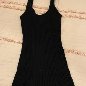 Svart ribbad klänning -  svart ribbad klänning med ärmlös design och rund hals. Perfekt för en stilren look. Den är helt oanvänd. Och är ganska så stretchig så den passar storlek S också.