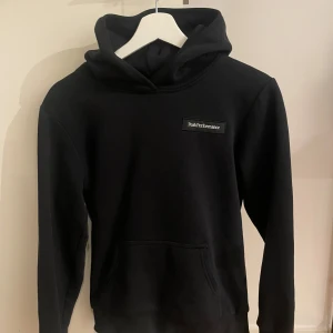 Svart hoodie från Peak Performance - Snygg svart hoodie från Peak Performance med logga på bröstet. Perfekt för en avslappnad stil. Den har en klassisk design med huva och långa ärmar.