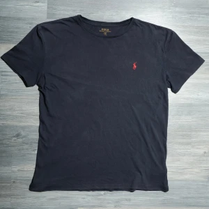 Mörkblå Ralph Lauren T-Shirt  - Säljer nu denna riktigt snygga Ralph Lauren T-shirten. Väldigt fint skick. Storlek S. Nypris ca 699kr, mitt pris endast 325kr. Hör av dig om du undrar något eller vill ha fler bilder! Pris är diskuterbart vid snabb affär🤝