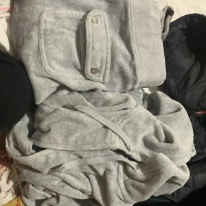 JUICY SET FÖR 550 - Säljer en mysig grå hoodie från Juicy Couture. Den har en praktisk ficka framtill med knappar och en dragkedja. Perfekt för en avslappnad stil.