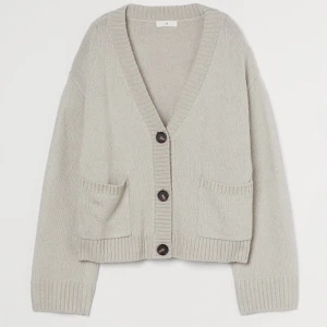 Beige kofta från H&M - Säljer en mysig beige kofta från H&M med stora knappar och två fickor framtill. Koftan har en djup v-ringning och ribbade kanter vid ärmslut och nederkant. Tröjan är väll använd 