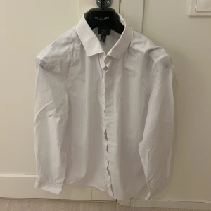 Vit skjorta från h&m - Klassisk vit skjorta från h&m i storlek M. Skjortan har en stilren design med knappar framtill och långa ärmar. Perfekt för både formella och avslappnade tillfällen.