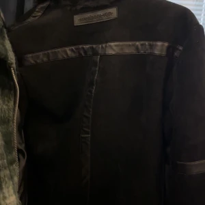 Svart jacka från Manière De Voir - Snygg svart jacka från Manière De Voir med dragkedja och pälsfoder. Jackan har läderdetaljer och flera fickor med dragkedjor. Perfekt för en stilren look.