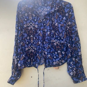 Blommig blus från Lindex - Säljer en superfin blommig blus från Lindex i storlek L. Den har ett härligt mönster i blått, vitt och orange med långa ärmar och knytband i nederkanten. Perfekt för både vardag och fest! 🌸