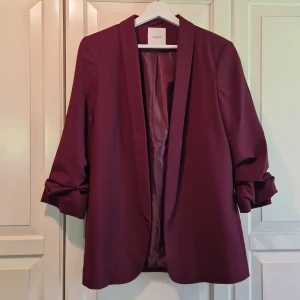 Vinröd kavaj från Pieces - Säljer en snygg vinröd kavaj från Pieces i storlek L. Den har en stilren design med trekvarts ärmar och en öppen framsida utan knappar. Perfekt för både vardag och fest!