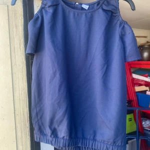 Mörkblå topp från Lindex Kids - Säljer en snygg mörkblå topp från Lindex Kids. Den har korta ärmar och en dragkedja i ryggen för en cool look. Perfekt för både vardag och fest!