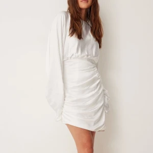 Vit klänning med långa ärmar - Säljer en superfin vit klänning med långa ärmar och en tight passform. Klänningen har en snygg omlott-detalj och är perfekt för festliga tillfällen. Materialet ser ut att vara mjukt och glansigt, vilket ger en lyxig känsla. Perfekt för vår och sommar!