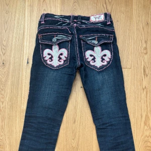 Fina raka jeans med rosa detaljer - Raka jeans med rosa sömmar och detaljer. Köpta på plick men var för stora. Bra skick, förutom att ena knappen lossnat på bakfickan hos tidigare ägare. midjemått - 37cm innerbensmått - 83cm grenhöjd - 21cm benöppning - 17cm