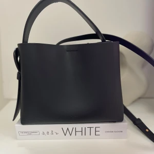 ARKET väska - Arket crossväska, storlek mellan. Man kan se lite flagning av ladret langs kanten av handtaget. Mätt 23 cm x 19 cm x 10,5 cm.