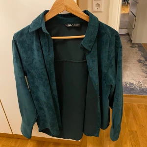 Grön overshirt från Zara - Snygg grön overshirt från Zara i mocka-look. Perfekt för lager-på-lager-stil med knappar framtill och klassisk krage. Passar bra till både vardag och mer uppklädda tillfällen.