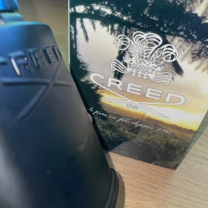 Creed Green Irish Tweed Parfym - Exklusiv parfym från Creed, Green Irish Tweed, i en elegant svart flaska med 120 ml innehåll. Flaskan har en stilren design med Creed-logotypen präglad på framsidan och ett dekorativt lock. Doften är känd för sina fräscha och naturliga toner.