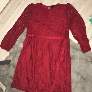 Röd spetsklänning från Mwear Woman - Säljer en elegant röd spetsklänning från Mwear Woman. Klänningen har trekvartsärmar och ett fint knytband i midjan. Klänningen ser lite större ut på bilden än vad den egentligen är.