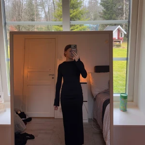 Svart långklänning med öppen rygg - Elegant svart långklänning med långärmad design och en stilfull öppen rygg med knytning. Aldrig använd så i toppen skick 