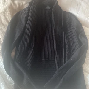 Svart ribbad kofta - Säljer en stilren svart kofta med ribbad design. Koftan har långa ärmar och en öppen front som ger en avslappnad look. Perfekt för lager-på-lager under kyligare dagar.