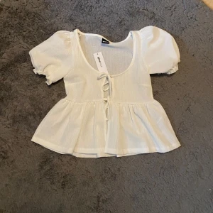 Offwhite ribbad topp med knytning - Säljer en söt offwhite ribbad topp med knytning framtill. Aldrig använd.