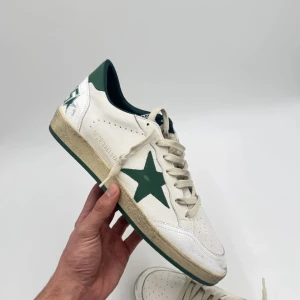 Vita sneakers med grön stjärna - (TAR BUD)Snygga vita sneakers från Golden Goose med en grön stjärna på sidan och gröna detaljer vid hälen. Skorna har snörning och en vintage-inspirerad sula. Perfekta för en avslappnad stil.