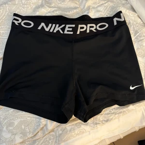 Svarta träningsshorts från Nike Pro - Säljer ett par svarta träningsshorts från Nike Pro. Shortsen har en elastisk midja med Nike Pro-logga och är perfekta för intensiva träningspass. De är designade för att ge en tight passform och maximal rörelsefrihet.