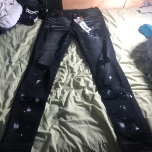 Svarta jeans med färgstänk från Purple Brand - Snygga svarta jeans från Purple Brand med unika vita färgstänk och slitna detaljer. De har en modern passform och är perfekta för en trendig look. Jeansen har en klassisk femficksdesign och en bekväm midwaist.