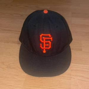 Svart keps från New Era - Snygg svart keps från New Era med orange broderad logga på framsidan. Kepsen är en del av MLB Authentic Collection och har en liten MLB-logga på baksidan. Perfekt för sportfantaster!