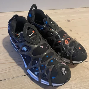 Nike sneakers med färgglatt mönster - Snygga Nike sneakers med ett unikt färgglatt mönster i svart, blått, orange och rosa. Skorna har en modern design med ett nätliknande överdrag och en liten Nike-logga på ovansidan. Perfekta för dig som vill sticka ut med stil.