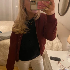 Vinröd bomberjacka - Säljer en snygg vinröd bomberjacka med dragkedja framtill. Jackan har en klassisk design med långa ärmar och ribbade muddar vid ärmslut och nederkant. Perfekt för en stilren look.