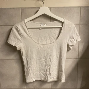 Vit kortärmad topp från H&M Divided - Säljer en enkel och stilren vit kortärmad topp från H&M Divided. Toppen har en rund halsringning och är perfekt för en avslappnad look. Passar bra till jeans eller kjol.