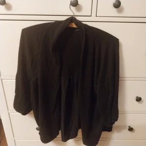 Kofta Svart - Säljer en stilren kofta. Den har en lös passform och trekvartsärmar, perfekt för en avslappnad men ändå elegant look. Materialet känns mjukt och bekvämt, vilket gör den lätt att bära hela dagen.