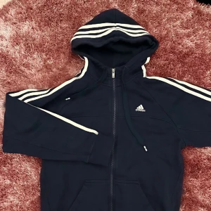 Marinblå huvtröja Adidas - Mörkblå huvtröja från Adidas med justerbar huva. Lite nopprig annars fint skick, strl S.