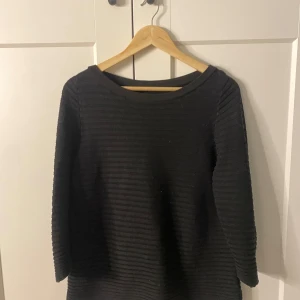 Svart ribbad tröja från COS - Säljer en stilren svart ribbad tröja från COS. Tröjan har trekvartsärmar och en rund halsringning, perfekt för en minimalistisk look. Passar bra till både jeans och kjol.
