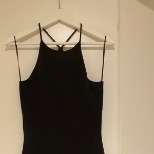 Svart klänning med smala axelband - Elegant svart klänning med smala axelband och en stilren design. Perfekt för en kväll ute eller en speciell tillställning. Klänningen har en figurnära passform som framhäver silhuetten.