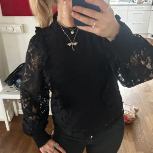 Svart spetsblus - Snygg svart blus med spetsdetaljer och långa ärmar. Perfekt för en elegant look med volangdetaljer på ärmarna. Passar bra till både jeans och kjol.