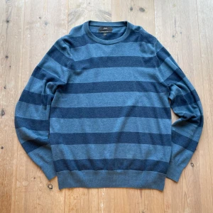 Blå och grå randig tröja från M&S - Säljer en stilren blå och grå randig tröja från M&S i ren bomull. Tröjan har långa ärmar och en klassisk rund halsringning. Hör av dig vid frågor!