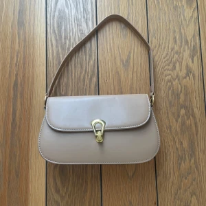 Beige axelväska med gulddetalj - Oanvänd fin handväska som också har ett längre band att ta på .