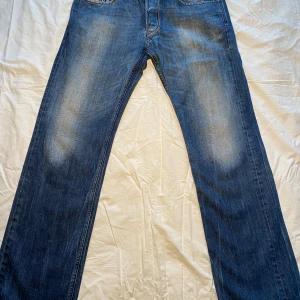 Blå jeans från Diesel - Snygga blå jeans från Diesel med klassisk femficksdesign och en cool tvättad look. De har en straight passform och är perfekta för en avslappnad stil. Märkesdetaljer syns på bakfickan och insidan av fickan.