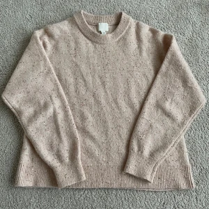 Rosa stickad tröja från H&M - Säljer en mysig beige stickad tröja från H&M med små glittriga detaljer. Tröjan har långa ärmar och ribbstickade muddar vid ärmslut och nederkant. Perfekt för kyliga dagar! Köpt från secondhand 