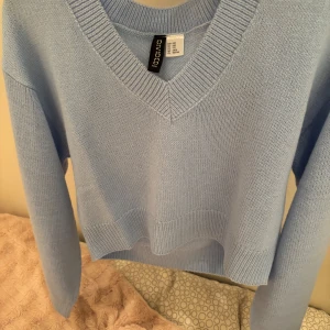 Ljusblå stickad tröja från H&M Divided - Säljer en ljusblå stickad tröja från H&M Divided. Tröjan har en v-ringad hals och är croppad med långa ärmar. Perfekt för en stilren och bekväm look. 💙