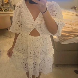 Studentklänning  - Vit broderad klänning med spets och volanger. Den har en v-ringad design och en öppen rygg med knytning. Klänningen är kort och har trekvartsärmar. Perfekt till studenten eller andra tillfällen😍