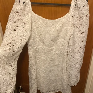 Vit spetsklänning - Säljer en elegant vit spetsklänning med långärmade detaljer. Klänningen har ett vackert blommigt mönster och en feminin passform. Perfekt för speciella tillfällen eller en romantisk kväll. 💫