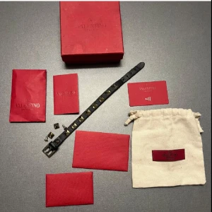 Svart armband med nitar från Valentino - Snyggt svart armband från Valentino med pyramidformade nitar. Armbandet har ett justerbart spänne och kommer i originalförpackning med tillhörande påse och kort. Perfekt accessoar för att ge en edgy touch till din stil.