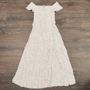 Vit prickig sommarklänning offshoulder - En vit offshoulder sommarklänning med svarta prickar, storlek 38 / M. Syns knappt men där finns en liten fläck på ryggen, se sista bilden. 