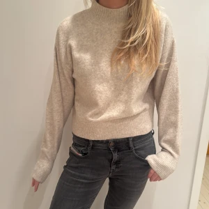 Beige stickad tröja från & Other Stories - Säljer en stilren beige stickad tröja från & Other Stories. Tröjan har en hög krage och långa ärmar med ribbade muddar. Perfekt för kyligare dagar och enkel att matcha med olika outfits.