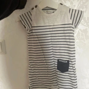 Randig jumpsuit från Newbie - Söt randig jumpsuit från Newbie i vitt och marinblått. Jumpsuiten har korta ärmar och knappar på axlarna för en fin detalj. Den har också en liten ficka med 'newbie' tryckt på. Perfekt för en avslappnad stil.