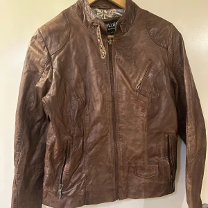 Brun skinnjacka från Collusion - Snygg brun skinnjacka från Hollies Stockholm med dragkedja framtill och flera praktiska fickor. Jackan har en stilren design med långa ärmar och en hög krage. Perfekt för en cool och avslappnad stil.