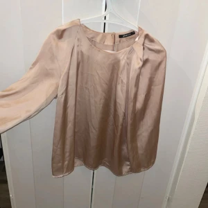 Stilren blus - Snygg långärmad blus  i rosé/guldig färg, blusen har en design med en liten öppning i nacken för en smickrande passform. Perfekt för en stilren look.