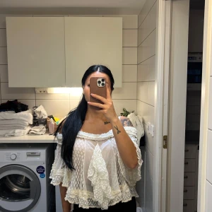 Vit offshoulder blus med volanger - Charmig vit offshoulder blus med volanger och spetsdetaljer. Perfekt för en somrig look med sin luftiga design och romantiska stil.