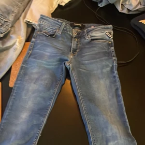 Blå jeans från Replay - Snygga blå jeans från Replay med klassisk femficksdesign och knappgylf. Perfekta för en avslappnad stil. Märkesdetaljer syns på baksidan och insidan av midjan.