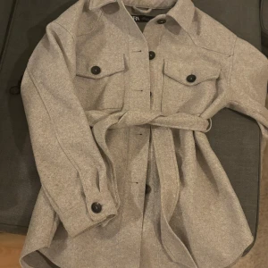 Grå kappa - Grå kappa med svarta knappar och bälte i midjan. Från zara 